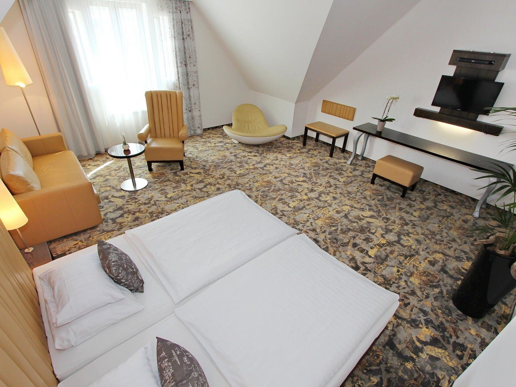 Ein Hotelzimmer mit einem großen Bett, zwei Sesseln, einer Couch, einem kleinen Tisch, einem Fernseher und einer Topfpflanze.