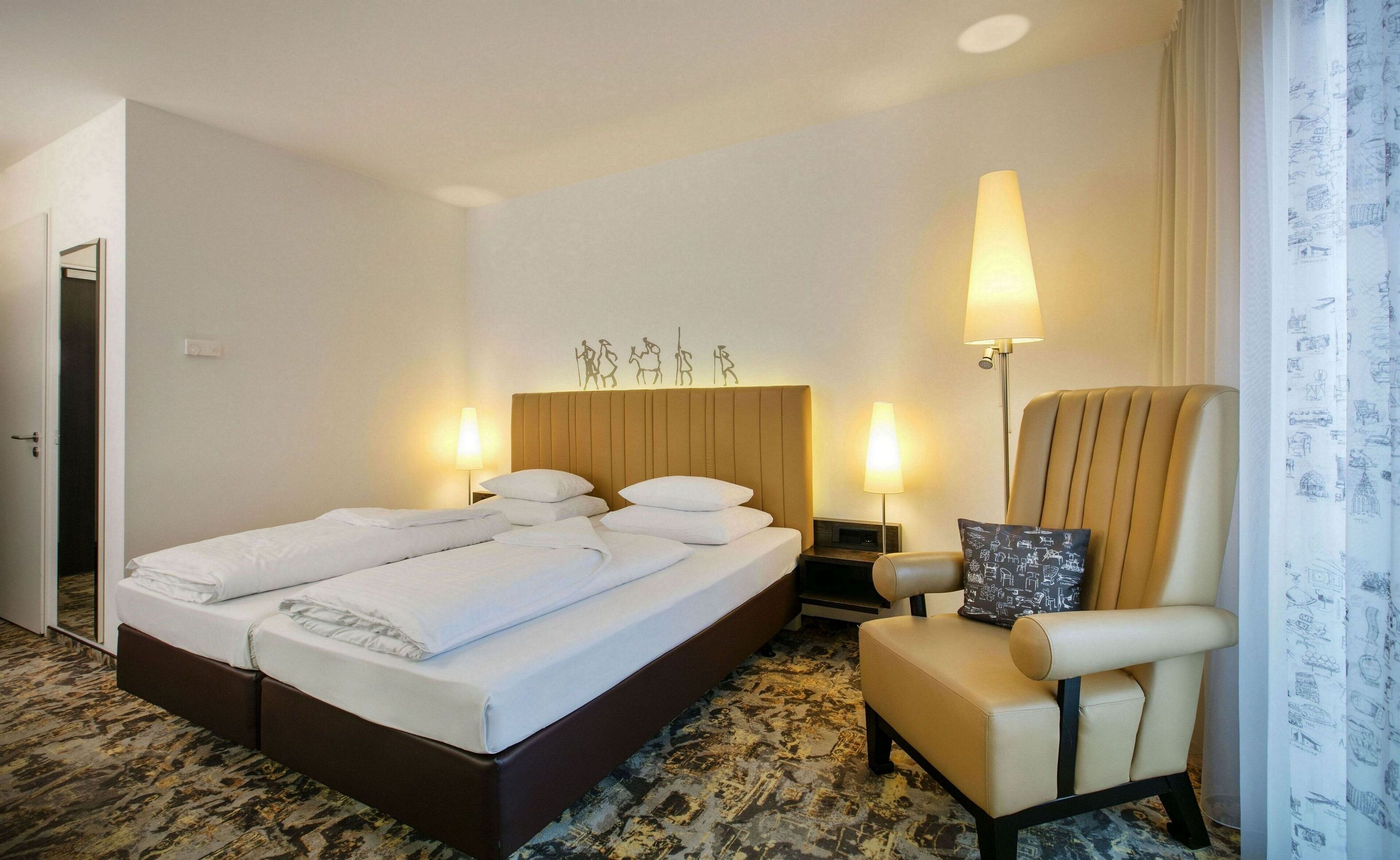 Habitación de hotel con cama, una silla, una mesita de noche y una pared decorada con un cabecero.
