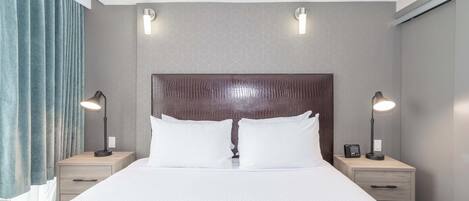 A modern hotel room with a large bed, two bedside tables with lamps, a headboard, and a geometric-patterned wall.