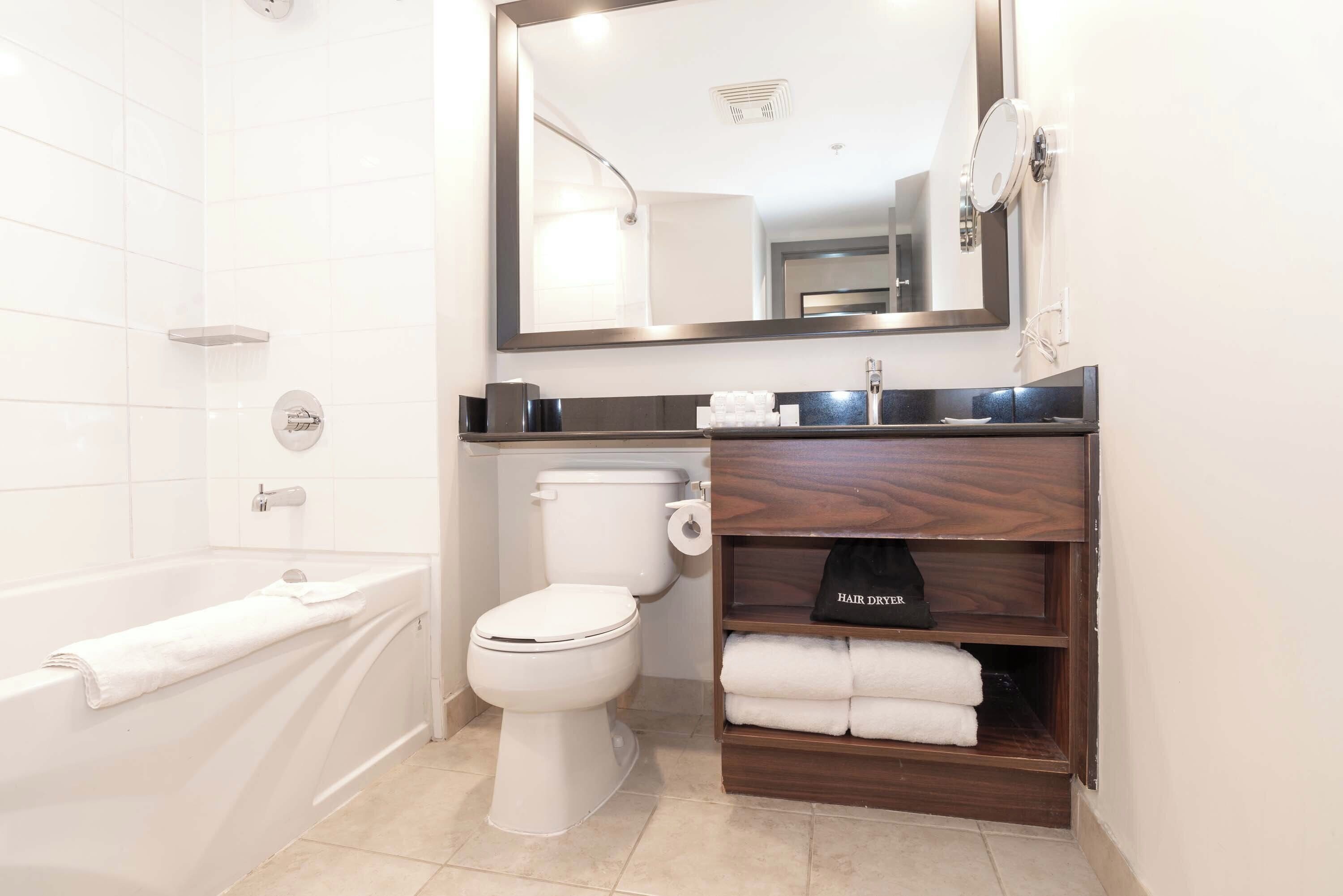 Een moderne badkamer met een witte badkuip, toilet en een wastafel met spiegel en handdoekhouder.