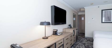 A hotel room with a bed, a desk with a lamp, a television, a coffee maker, and a telephone.