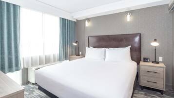 Quarto de hotel com uma cama grande, duas mesas de cabeceira com luminárias, um criado-mudo e uma janela com cortinas.