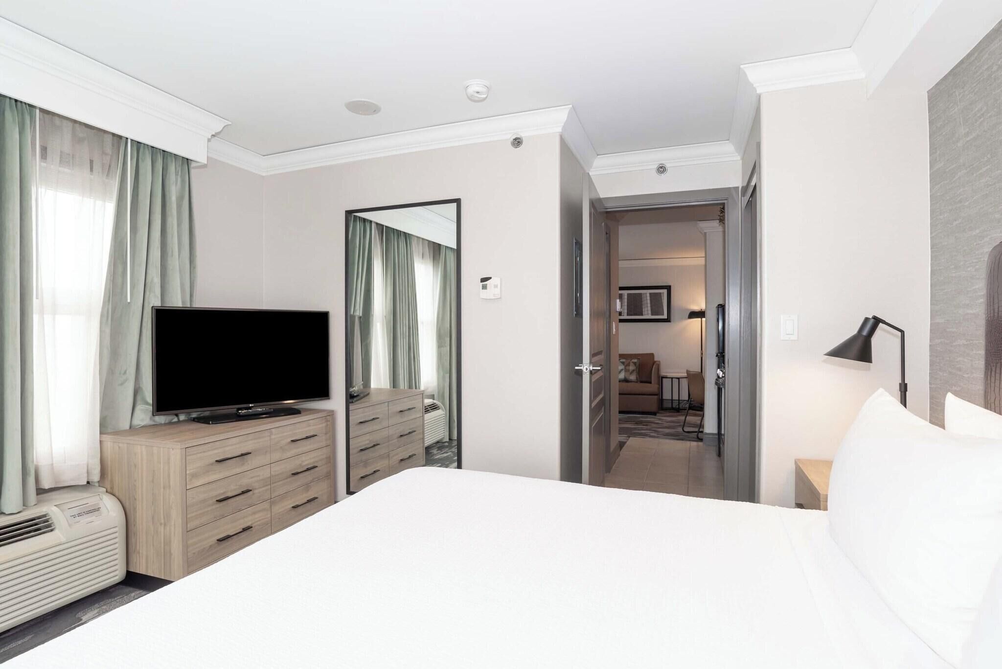 A hotel room with a bed, a TV on a dresser, a mirror, and a door leading to a bathroom.
