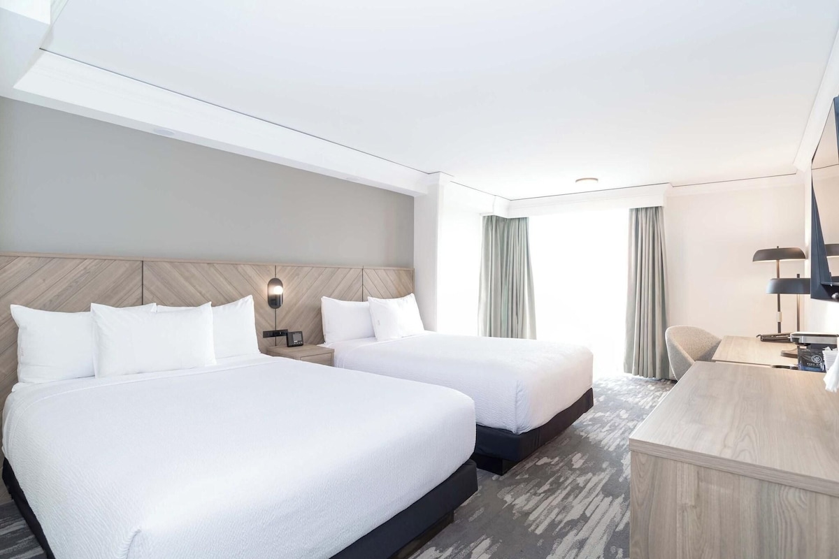 Een hotelkamer met twee bedden, een bureau, een stoel en een televisie.