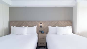 A hotel room with two beds, a wooden headboard, a nightstand with a clock, and a modern light fixture.