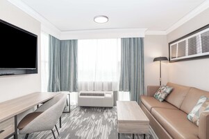 Una habitación de hotel moderna con una televisión de pantalla plana, un escritorio, un sofá y un gran ventanal con cortinas.