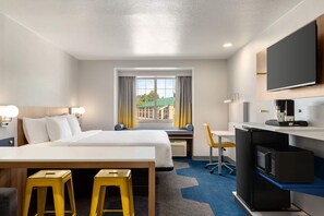 A hotel room with a bed, desk, TV, minibar, and a view of buildings. - Microtel Inn & Suites by Wyndham Culpeper (Culpeper)