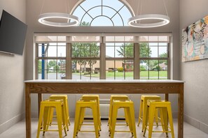 A room with a large window, a wooden table, and four yellow stools. - Microtel Inn & Suites by Wyndham Culpeper (Culpeper)
