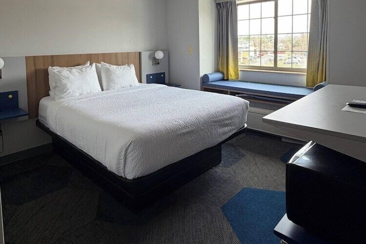 Ein Hotelzimmer mit Bett, Schreibtisch, einem Fenster mit Vorhängen und einer Deckenleuchte.