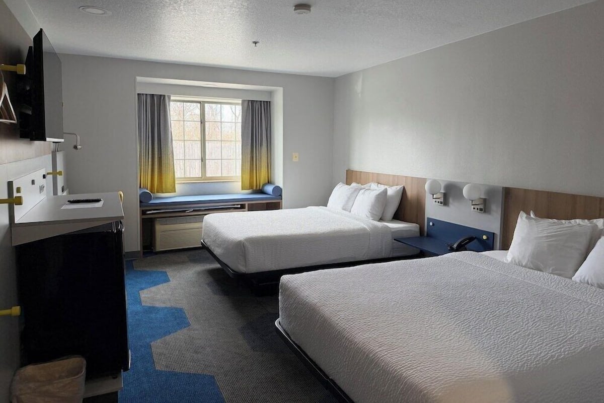 Ein Hotelzimmer mit zwei Betten, einem Schreibtisch, einem Fenster mit Vorhängen und einer Deckenleuchte.