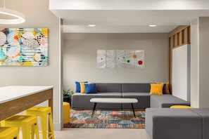 Una sala de estar moderna con un sofá gris, taburetes amarillos, una mesa blanca y arte abstracto en la pared.