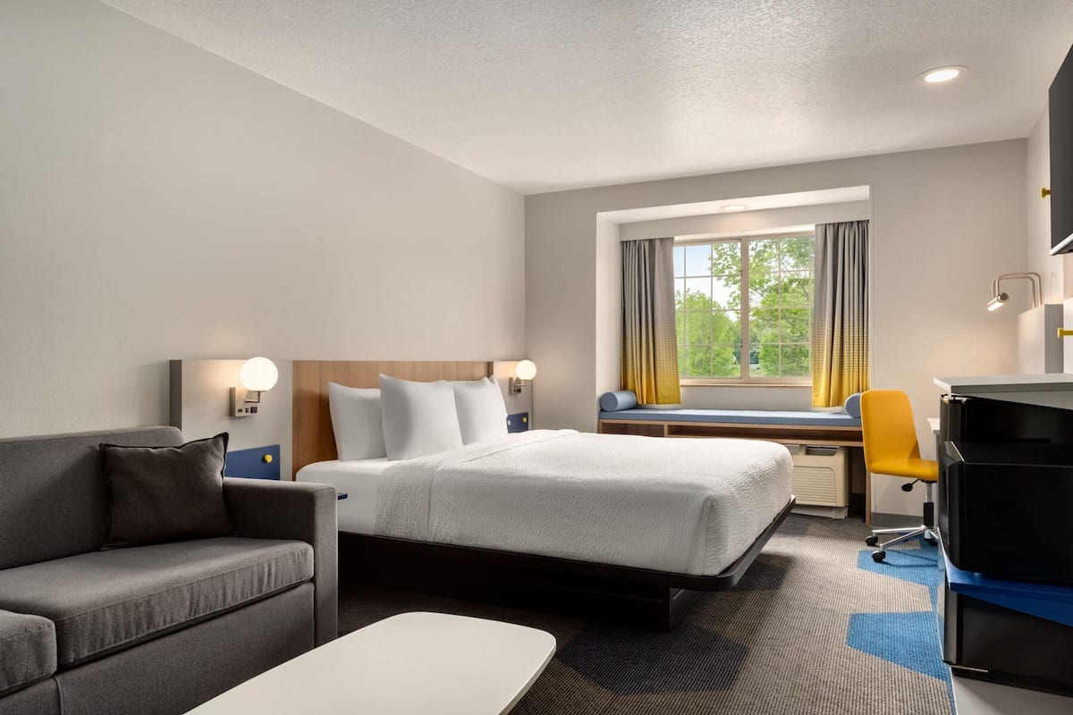Ein Hotelzimmer mit Bett, Schreibtisch, Sessel, Sofa und Fernseher.