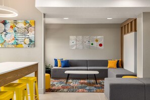 A modern living room with a gray sofa, yellow stools, a white table, and abstract wall art. - Microtel Inn & Suites by Wyndham Culpeper (Culpeper)