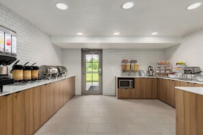 A modern kitchen with white tiled walls, wooden cabinets, a coffee station, and a view through a glass door. - Microtel Inn & Suites by Wyndham Culpeper (Culpeper)