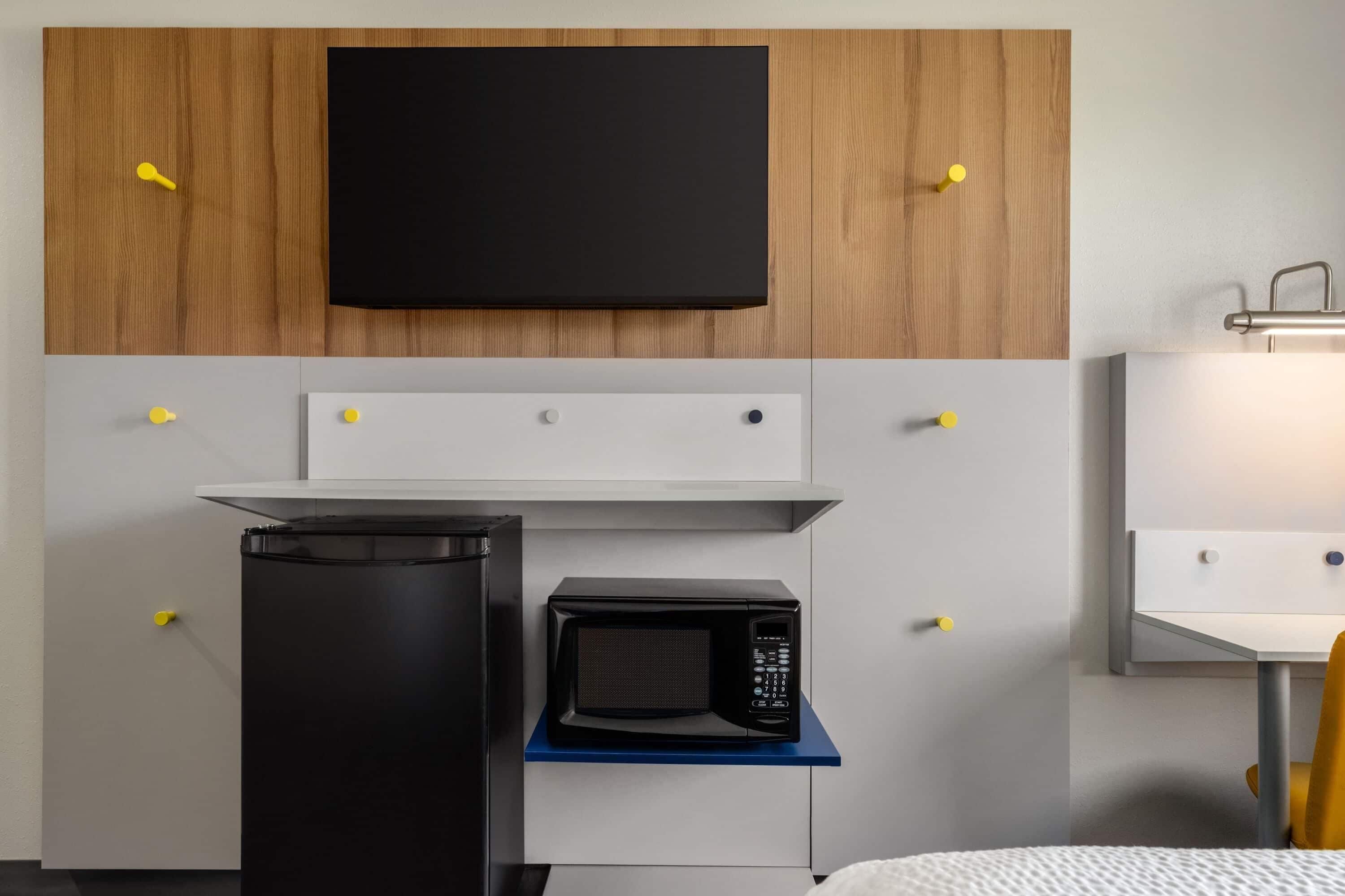 A compact kitchenette with a microwave, a small refrigerator, and a flat-screen TV mounted above the counter.