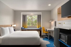 Habitación de hotel con cama, escritorio, silla, televisor y ventana con cortinas.
