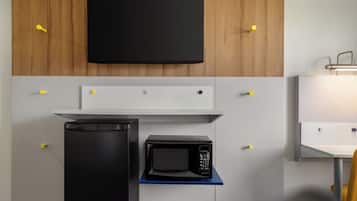 A compact kitchenette with a microwave, a small fridge, and a flat-screen TV mounted on a wooden wall.
