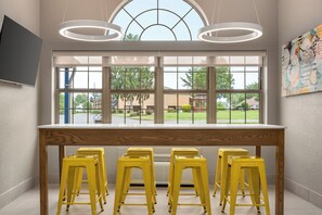 Una habitación con un ventanal grande, una mesa y cuatro taburetes amarillos.