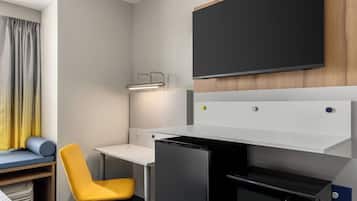 Ein kompaktes Hotelzimmer mit einem Bett, einem kleinen Schreibtisch, einem Stuhl, einer Mikrowelle und einem Fernseher.