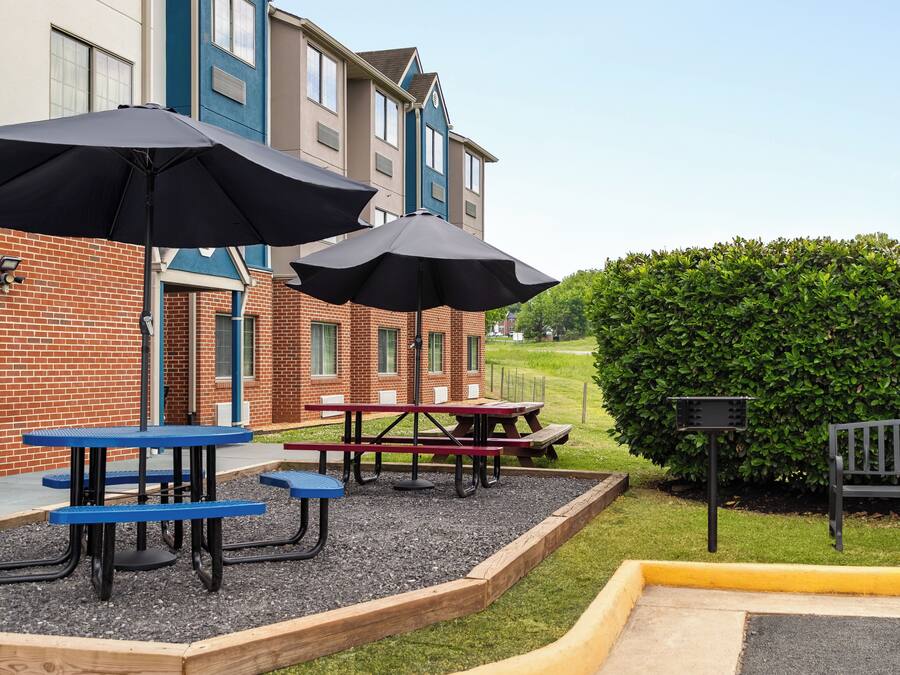 A patio area with picnic tables and umbrellas, a brick building, and a hedge.