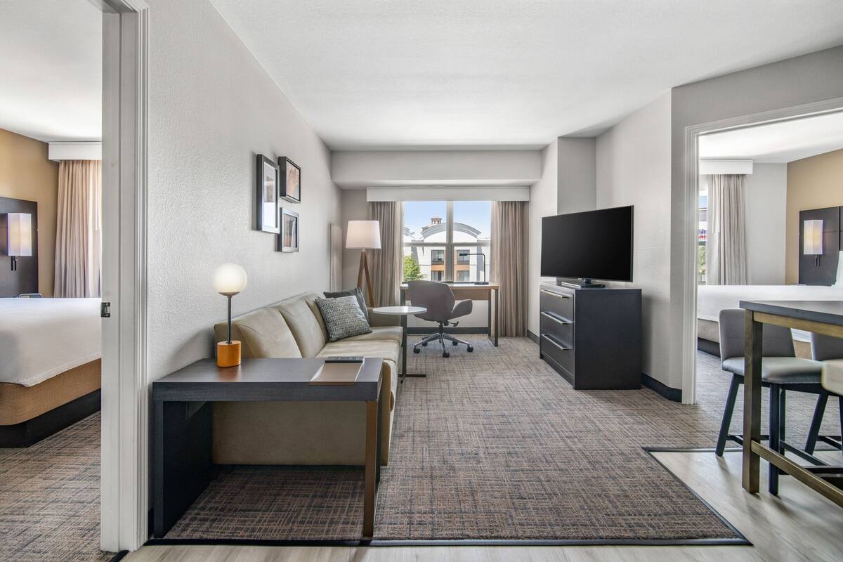 A hotel room with a bed, a sofa, a desk, a TV, and a view of the outside.