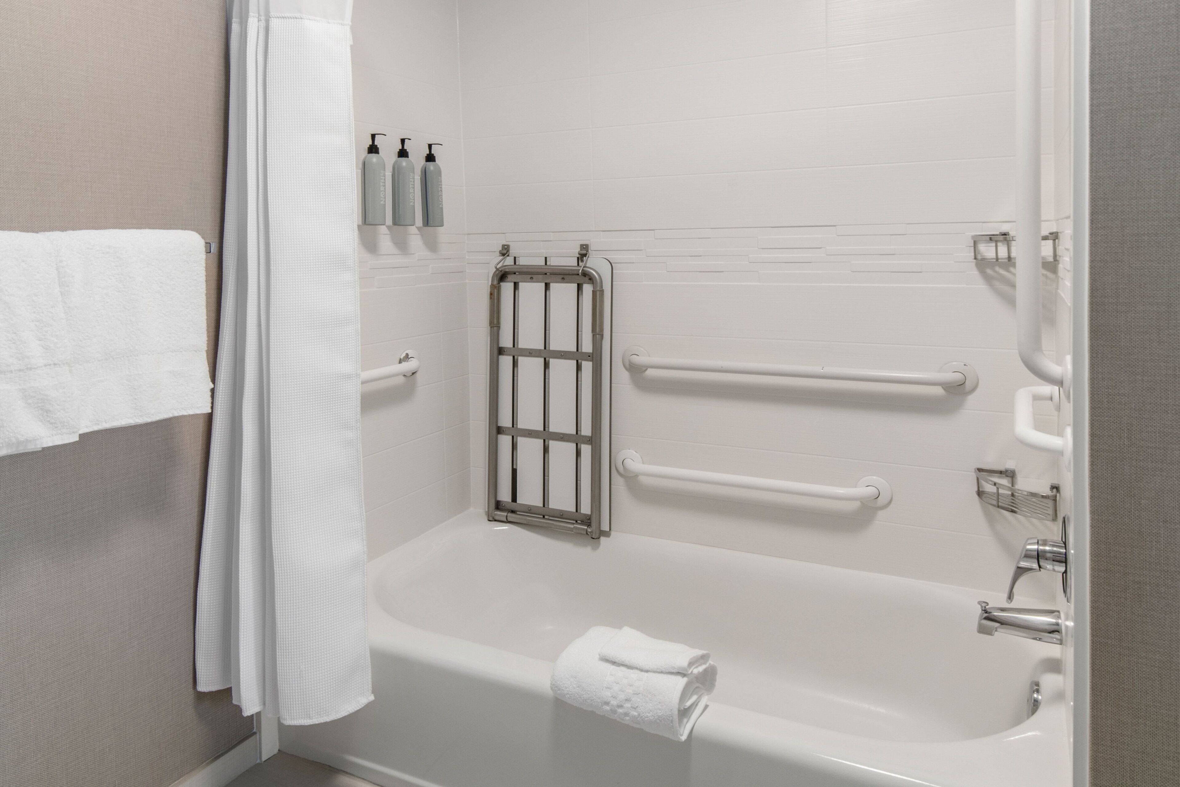 Un baño moderno con una bañera blanca, barras de apoyo y un perchero.