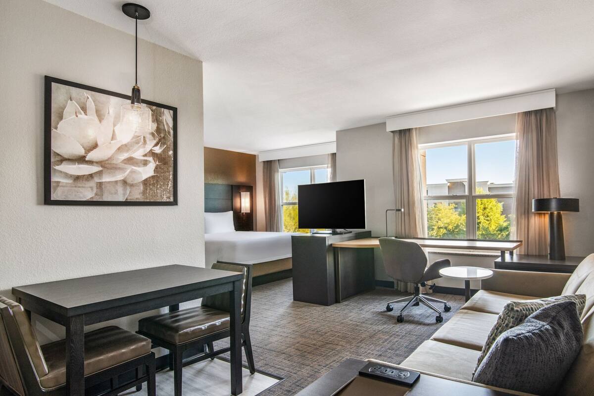 A hotel room with a bed, a desk, a TV, a sofa, and a dining table.