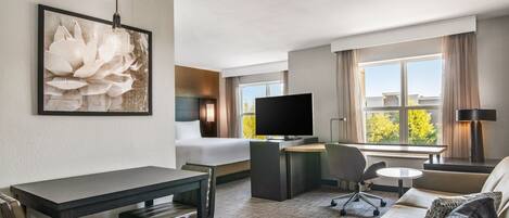A hotel room with a bed, a desk, a TV, a sofa, and a dining table.