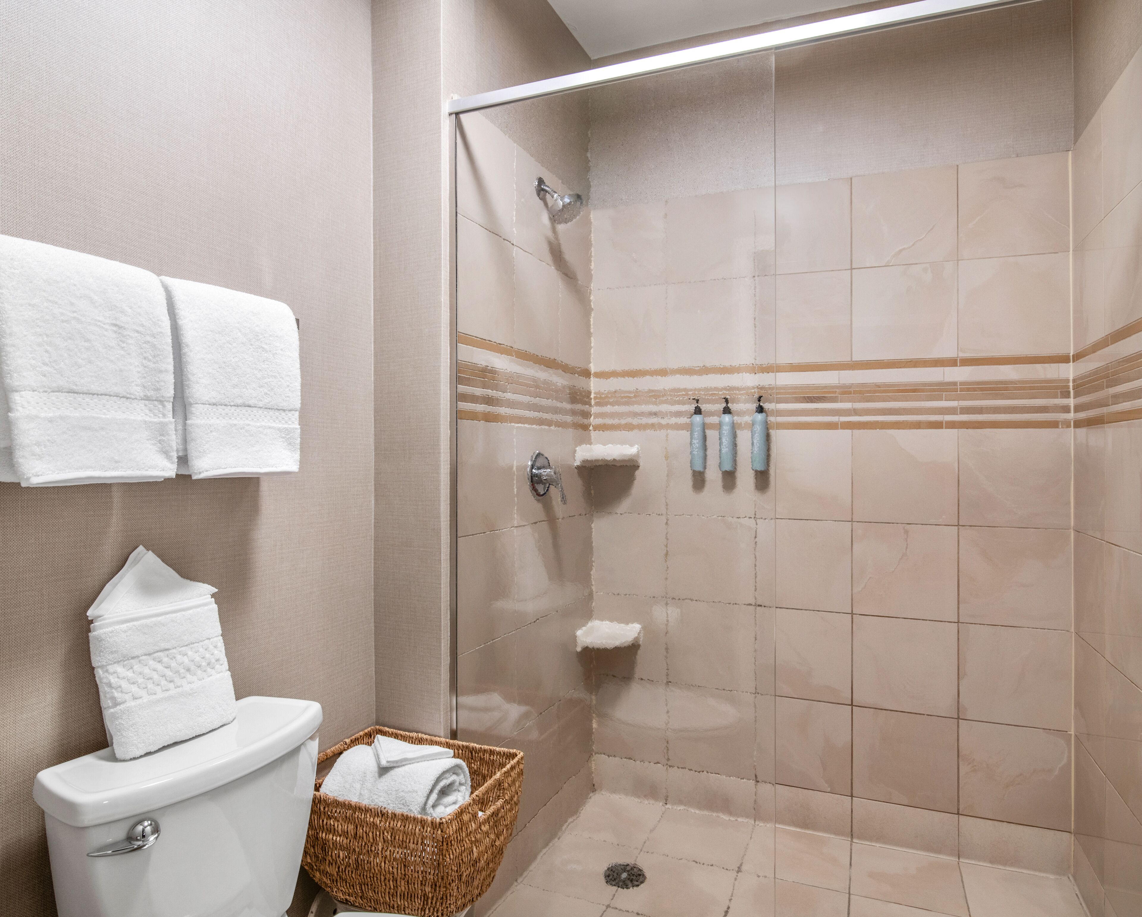 A bathroom with a toilet, a shower stall, and a wicker basket with towels.