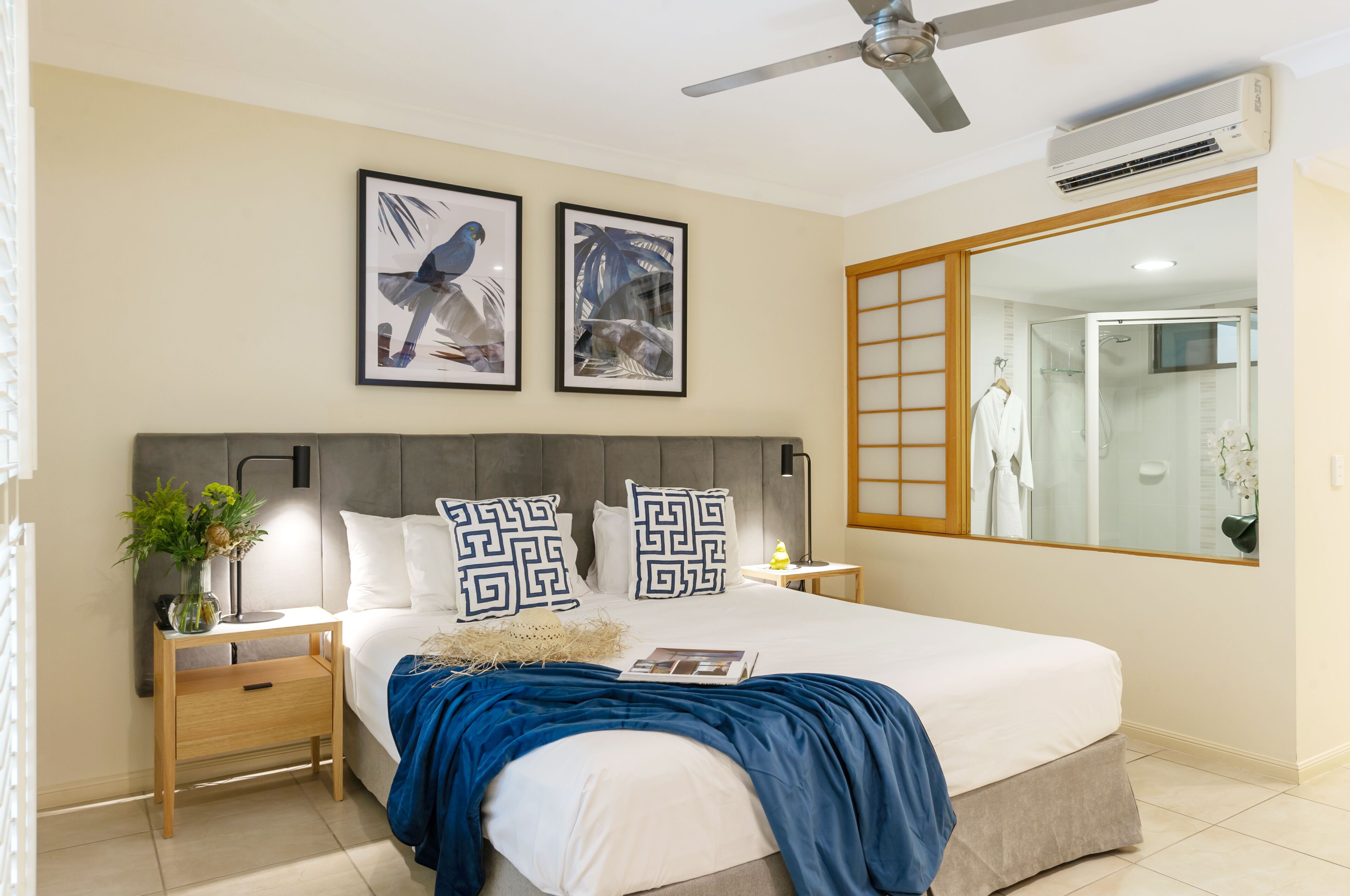 A bedroom with a bed, bedside tables, a ceiling fan, an air conditioner, and framed artwork on the wall.