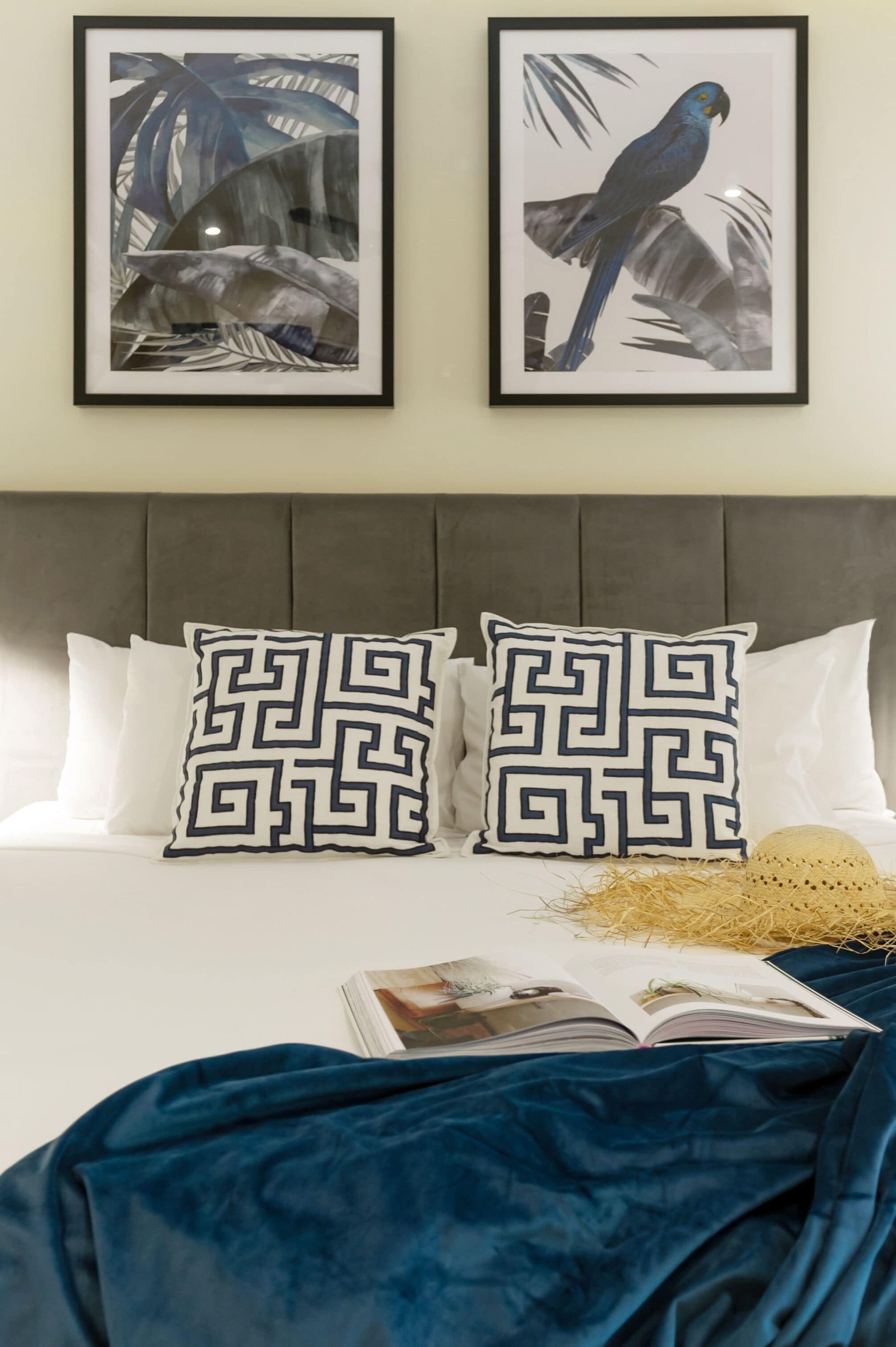 A bed with a dark blue blanket, two decorative pillows with a geometric pattern, and a framed artwork of a bird on the wall above.