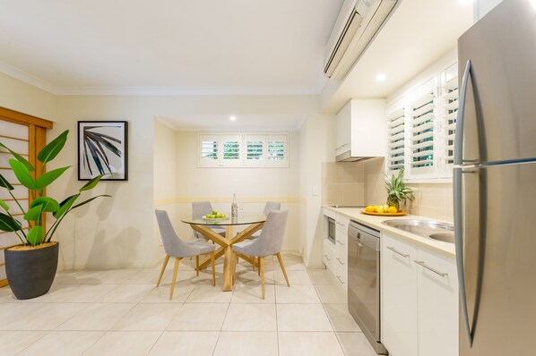 A modern kitchen with a dining area, featuring a stainless steel refrigerator, white cabinets, and a potted plant. - Shantara Resort Port Douglas - Adults Only Retreat (Port Douglas)