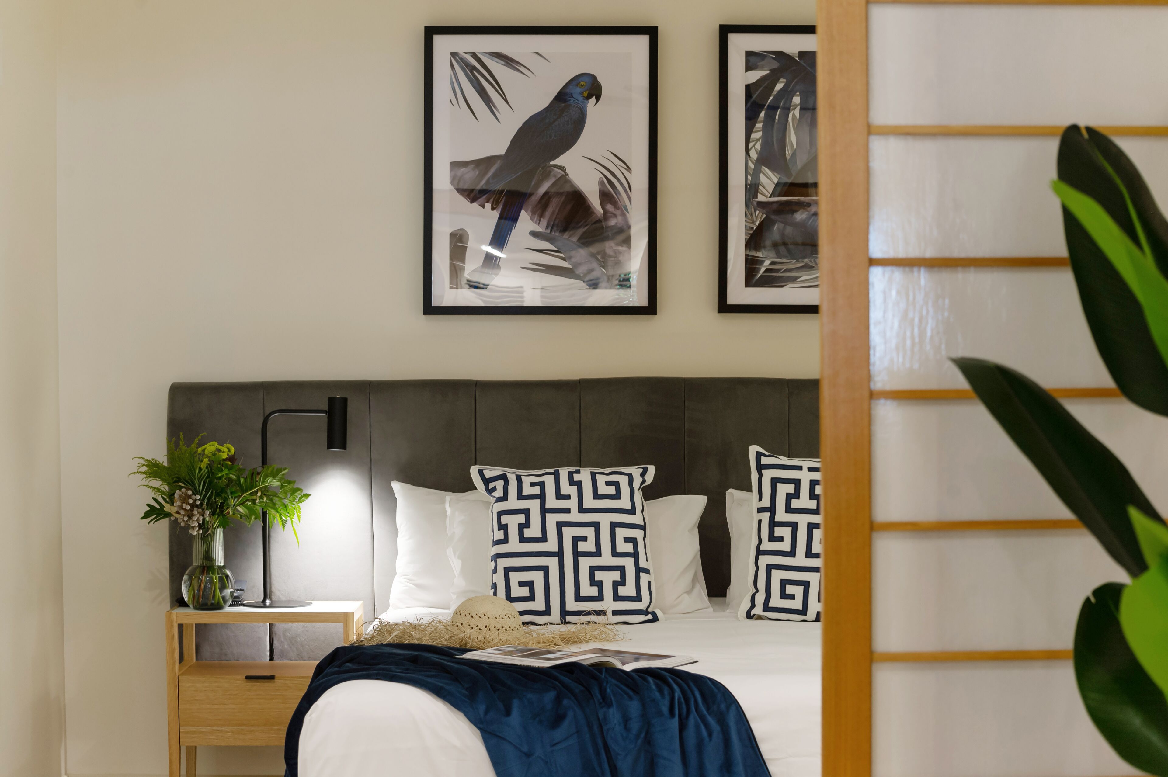 A bedroom with a bed, a nightstand with a lamp, a vase with flowers, and two framed pictures on the wall.
