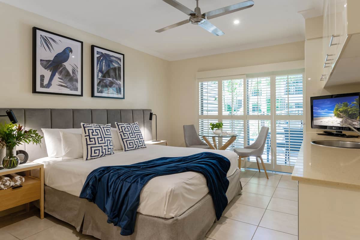 A modern bedroom with a bed, a ceiling fan, a TV, and a dining area with a chair and table.