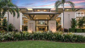 Un moderno edificio de resort con entrada central, varios balcones y un jardín bien cuidado.