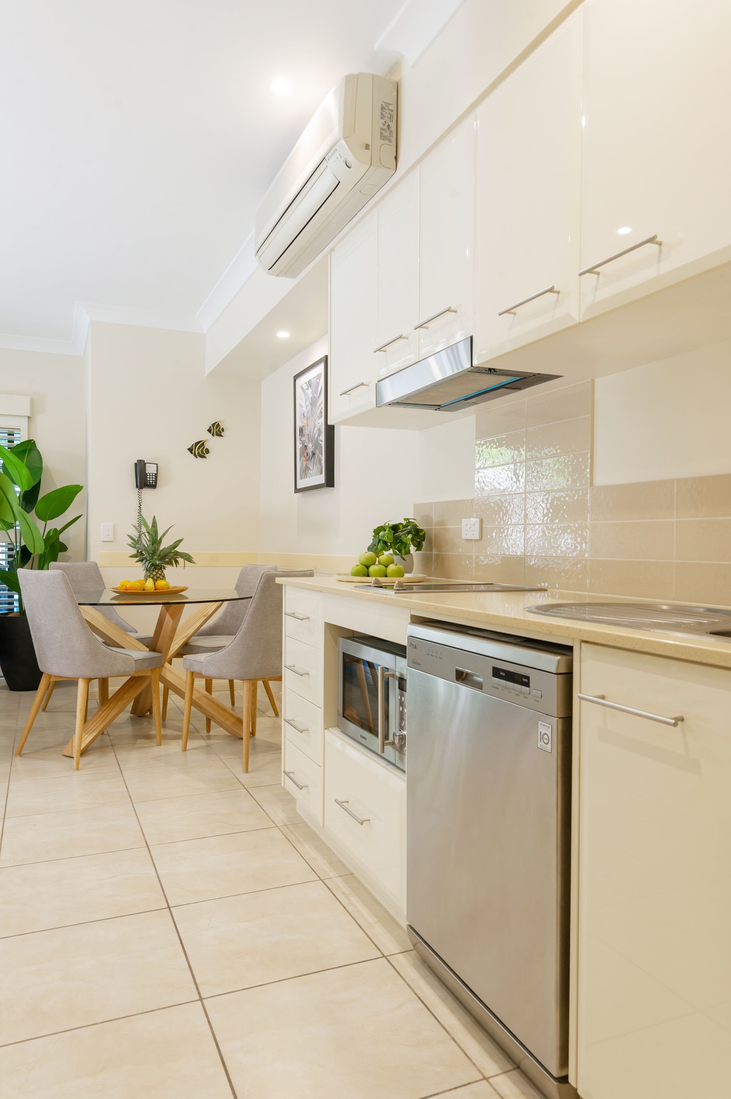 A modern kitchen with white cabinetry, a stainless steel dishwasher, and a glass dining table with chairs.
