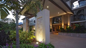 Entrada de hotel con pared de piedra, plantas de interior y un camino bien iluminado.