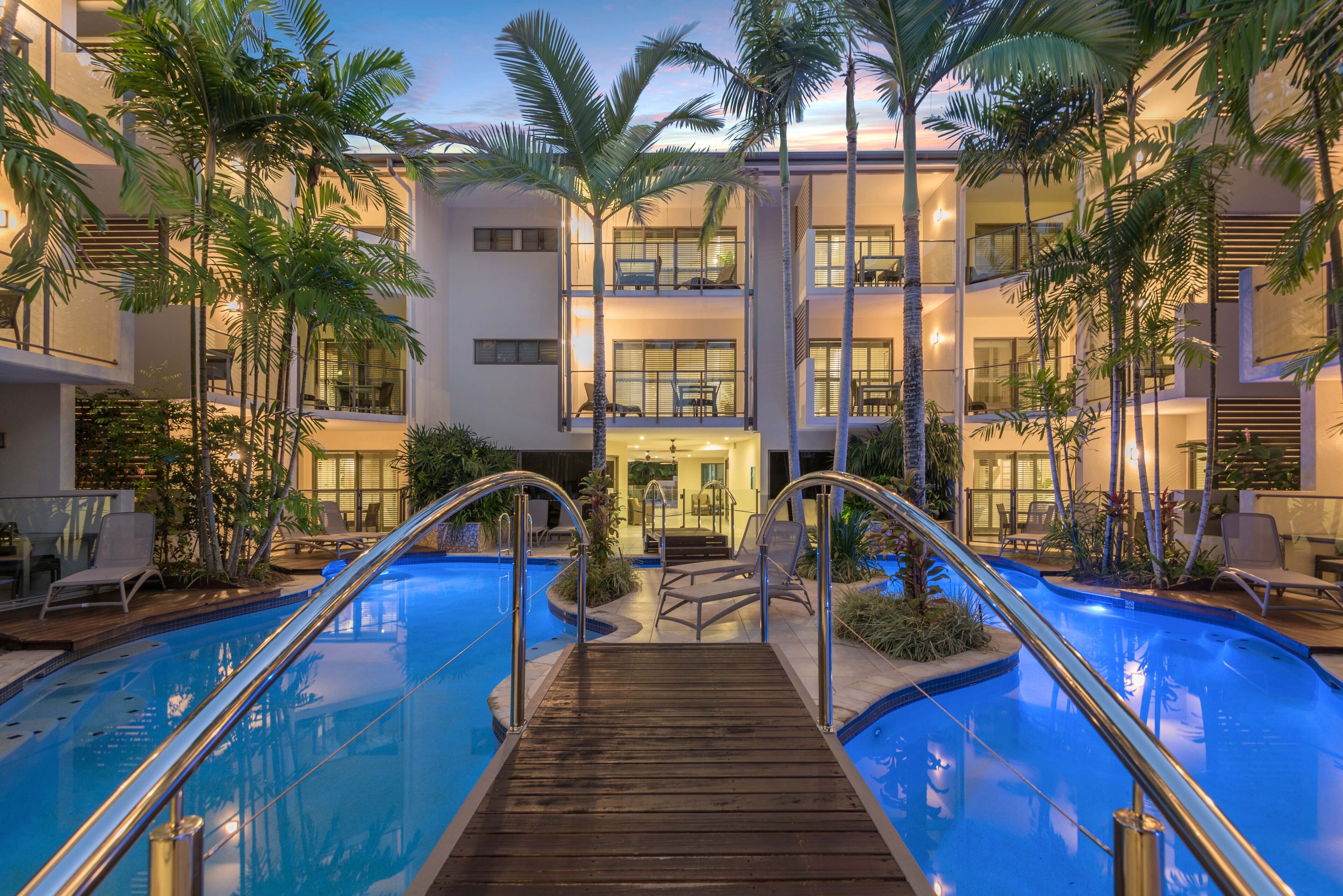 A multi-story hotel with a central pool area, palm trees, and outdoor seating.