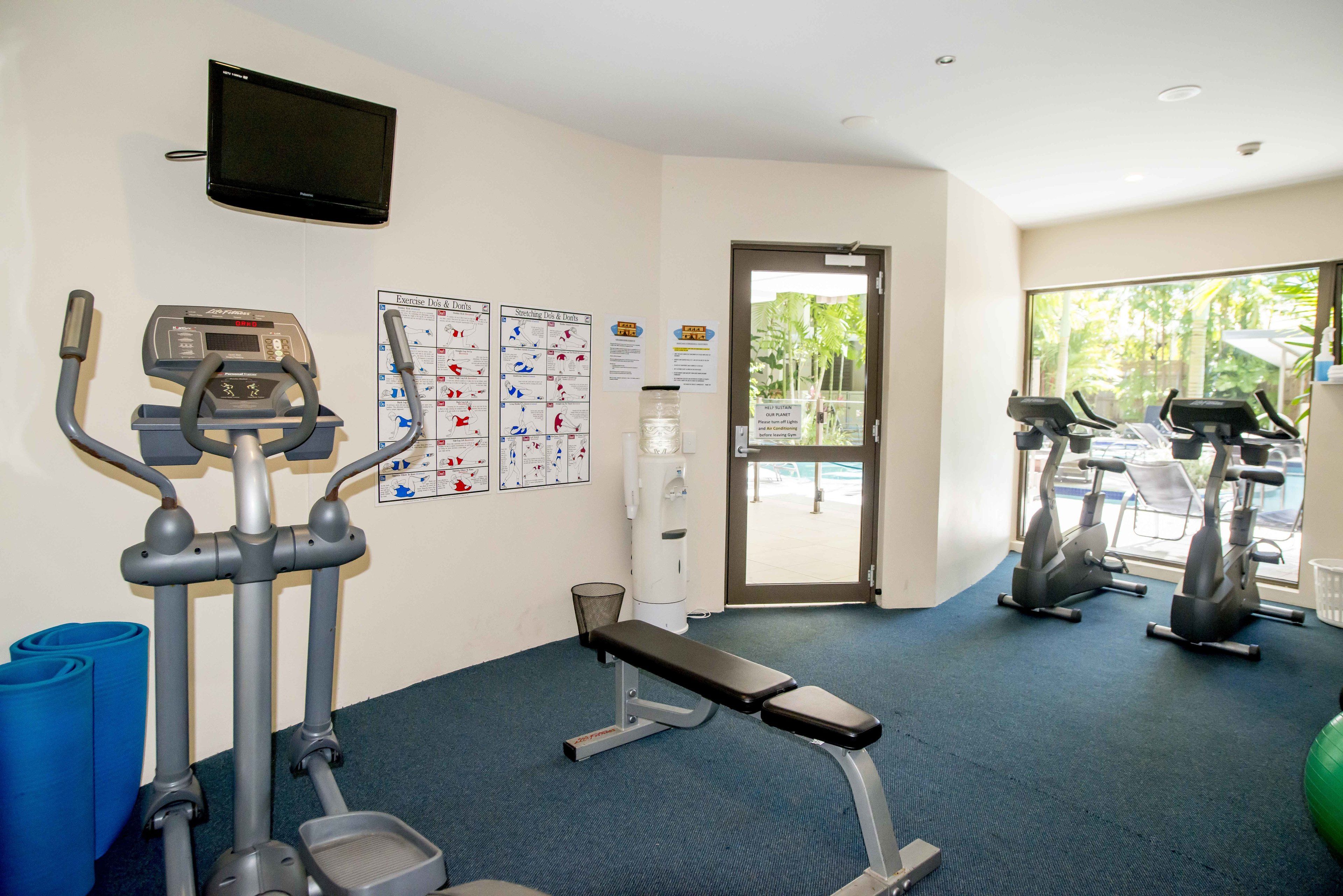 A gym with cardio machines, a bench, and exercise posters on the wall.