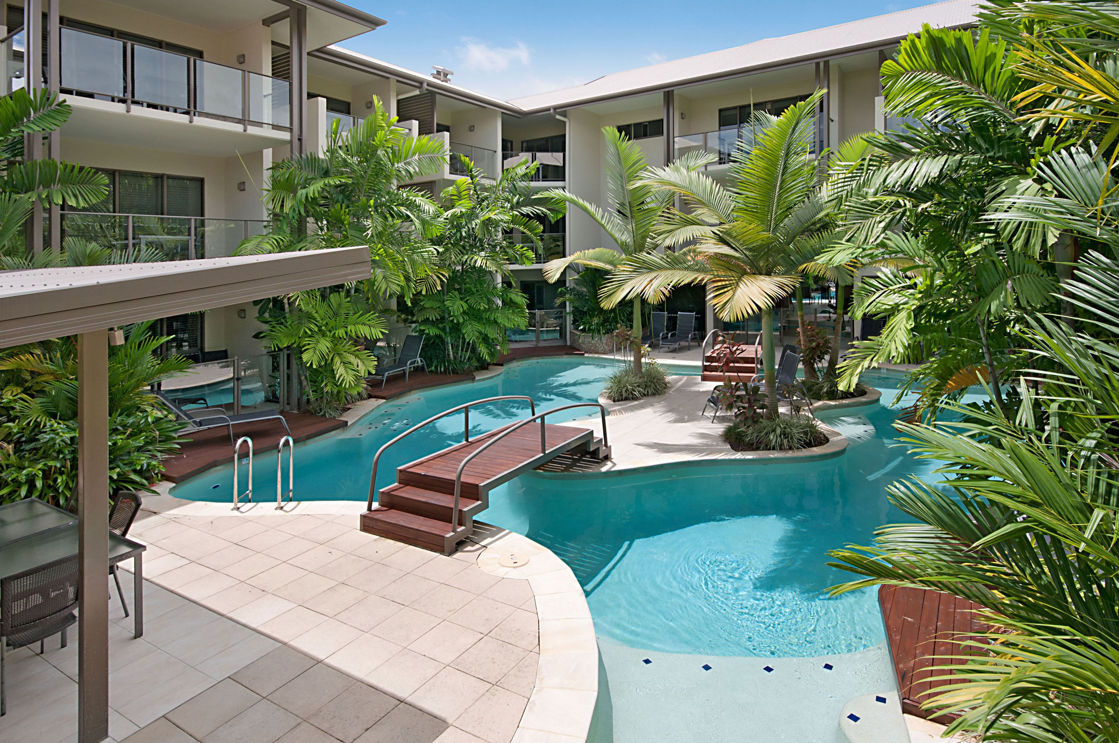 A hotel with a swimming pool surrounded by lush greenery, a covered seating area, and multiple balconies.