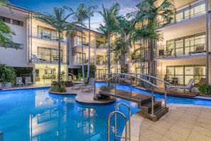 Un hôtel à plusieurs étages doté d’une piscine centrale, d’un espace extérieur aménagé et de palmiers.