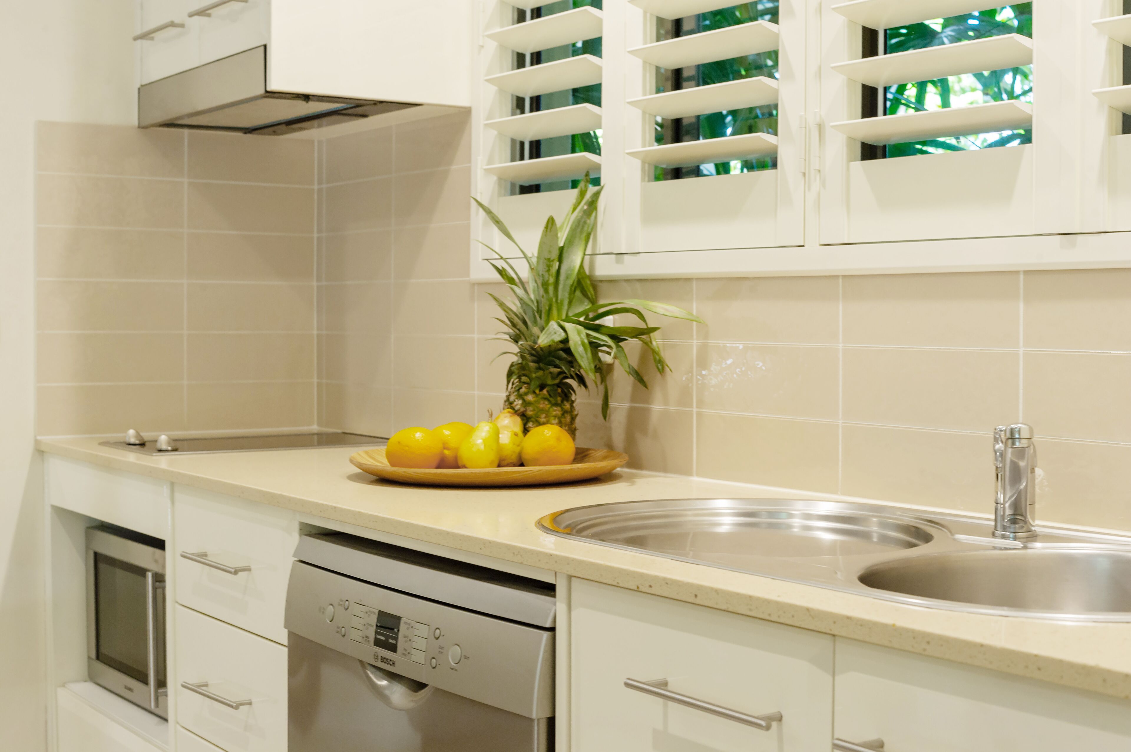 Una cocina con gabinetes blancos, un lavamanos de acero inoxidable y un escurreplatos.
