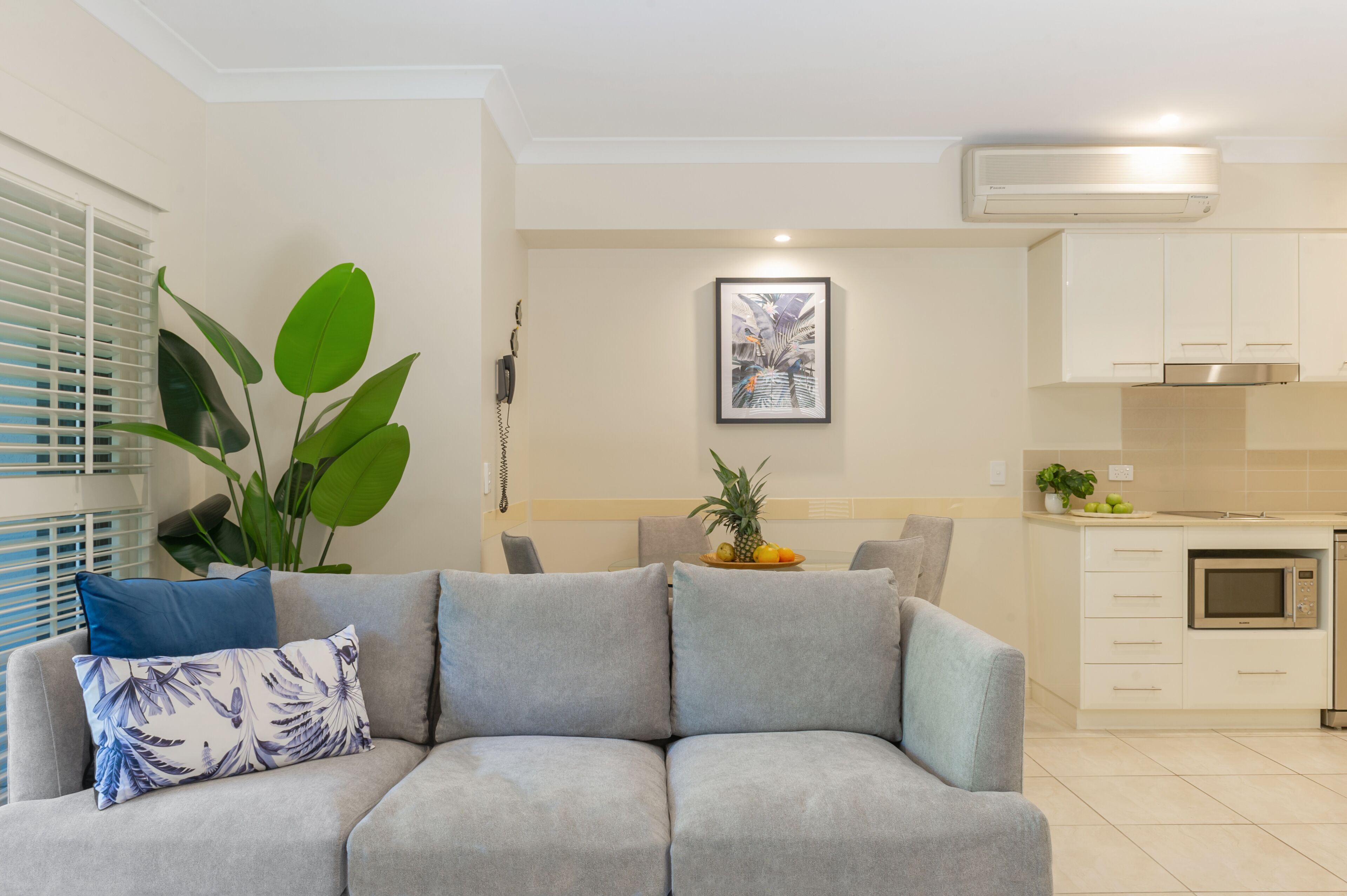 Una sala de estar moderna con un sofá gris, una planta verde grande y un cuadro en la pared.