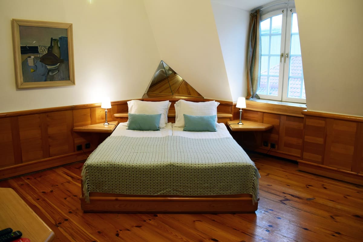 Ein Schlafzimmer mit einem hölzernen Bett, zwei Nachttischen mit Lampen, einem Bild an der Wand und einem Fenster mit Vorhängen.