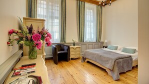 A bedroom with a bed, a desk with a chair, a dresser, and a vase of flowers. - Boutique Hotel KRISTOFS (Riga)