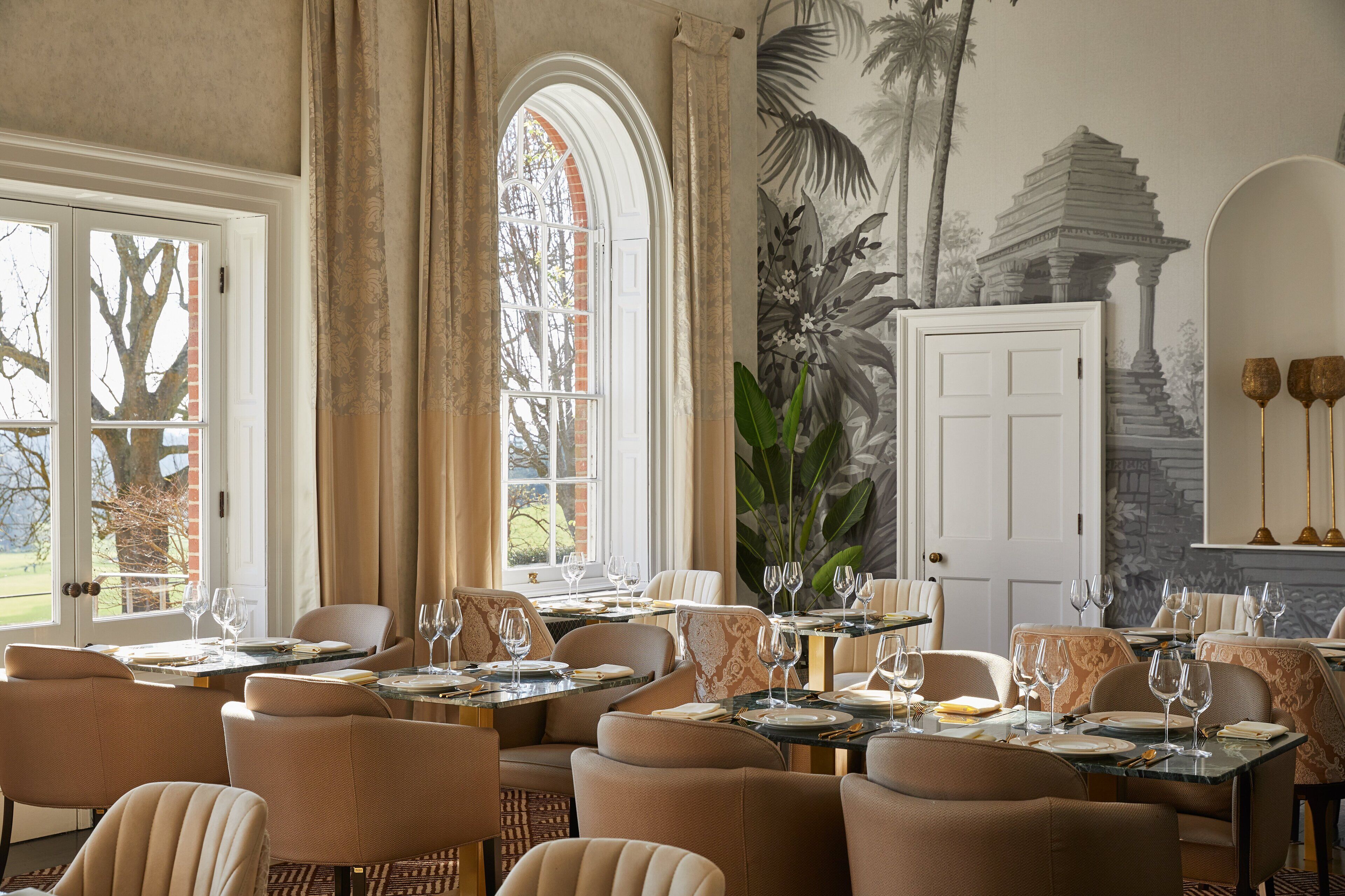 Un espace repas avec des tables dressées pour le service, de grandes fenêtres et une fresque murale.