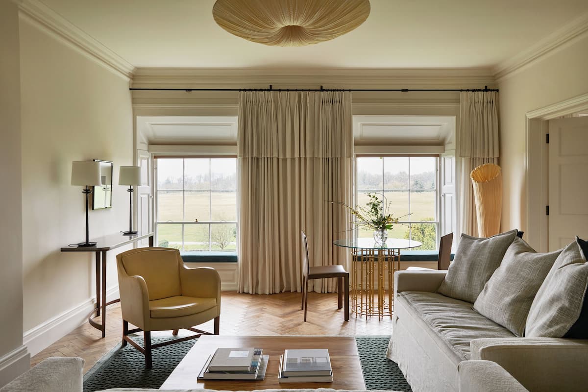 A living room with a sofa, armchair, coffee table, and a view of a garden through large windows.