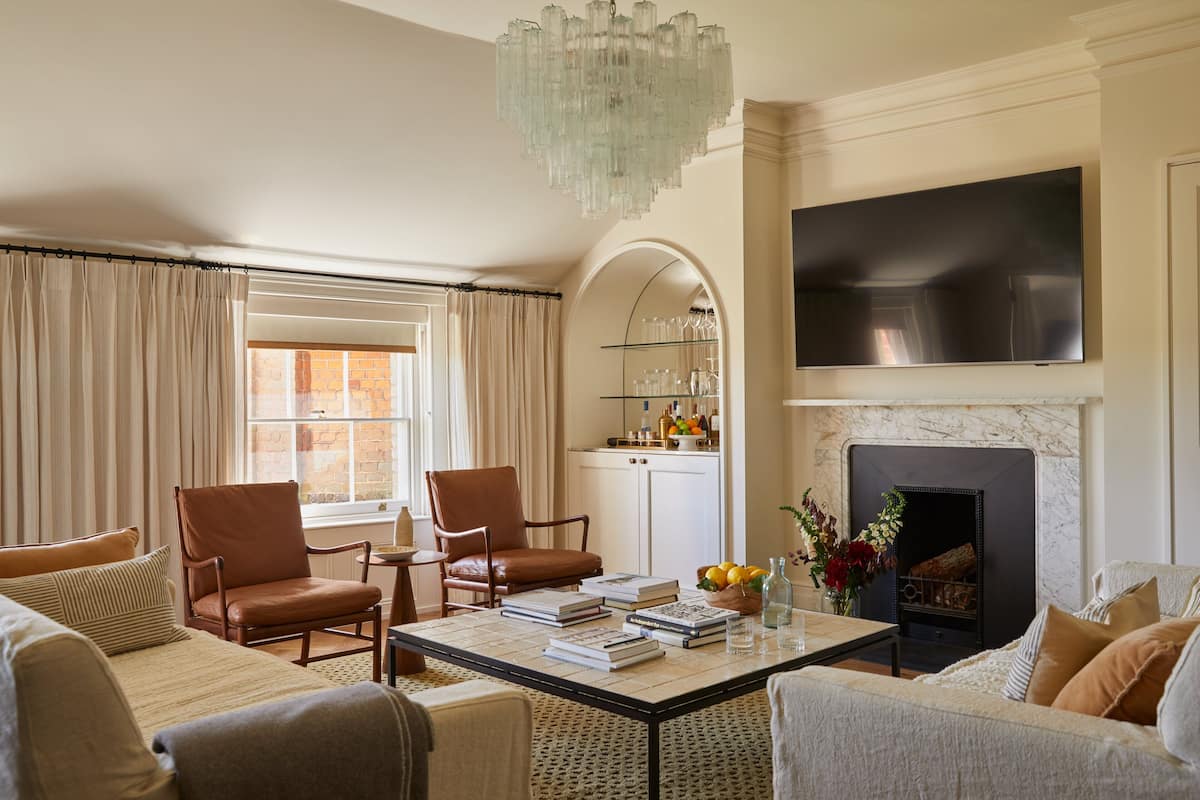 A living room with a fireplace, a television mounted on the wall, and a coffee table with books and a vase of flowers.