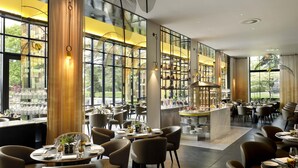 A modern restaurant with large windows, round tables, and contemporary chairs.