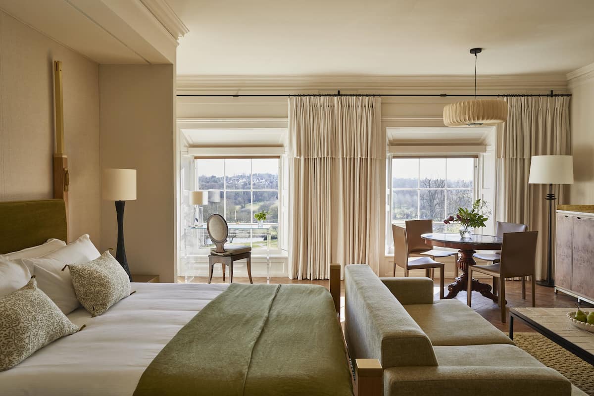 A hotel room with a large bed, a sofa, a dining table with chairs, and a view of the outdoors.